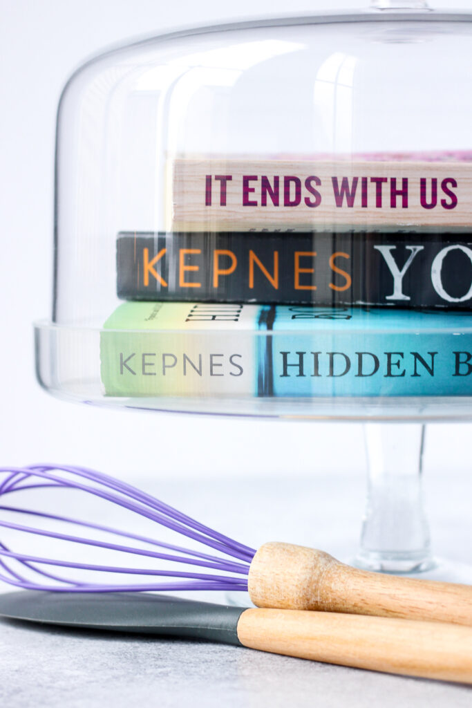 Books in a glass dessert stand with a whisk and spatula
