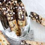 S'mores Biscotti in a tin with several biscotti scattered around it