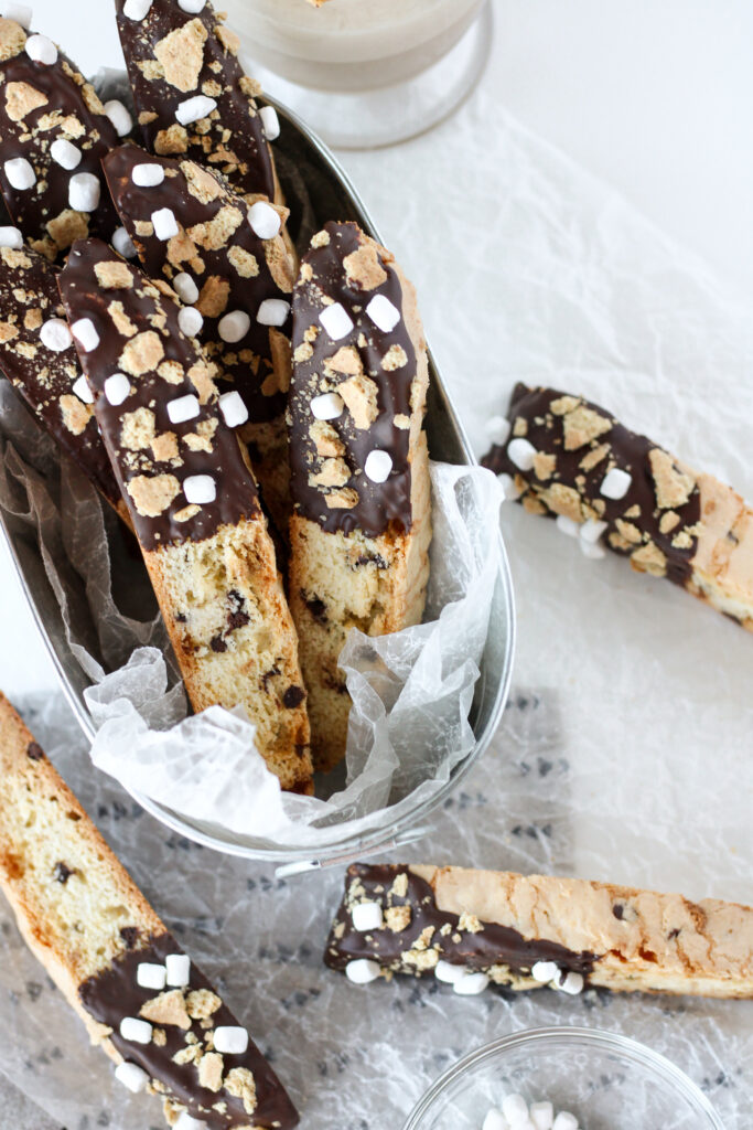 S'mores Biscotti in a tin with several biscotti scattered around it