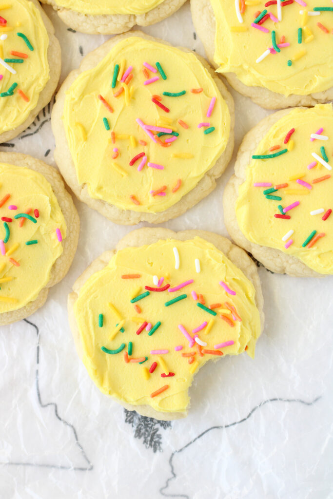 Lofthouse style sugar cookies with yellow frosting and rainbow sprinkles