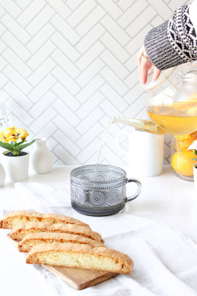 Pouring tea into a mug. Biscotti in the foreground.