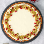 Honey, Goat Cheese, and Pistachio Tart topped with crushed pistachios and pomegranate arils on a slate serving platter.