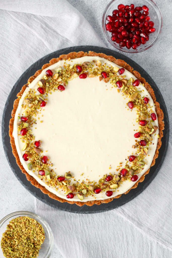 Honey, Goat Cheese, and Pistachio Tart topped with crushed pistachios and pomegranate arils on a slate serving platter.