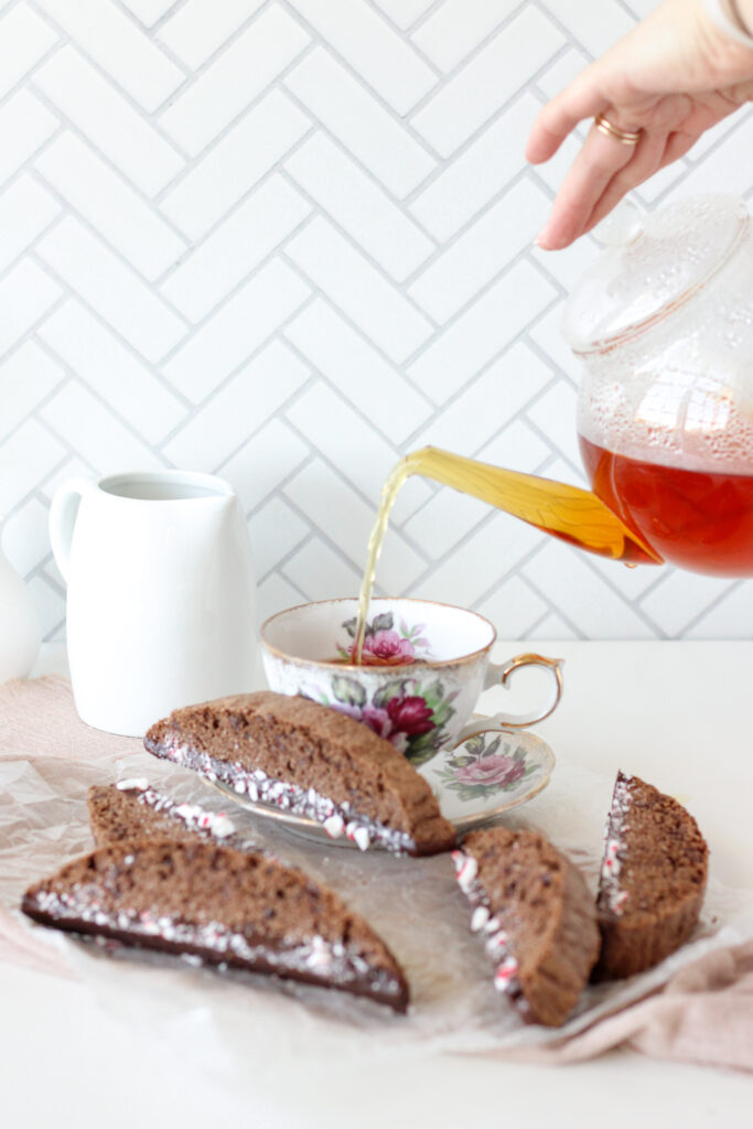 Pouring tea into a teacup with chocolate peppermint biscotti in the foreground