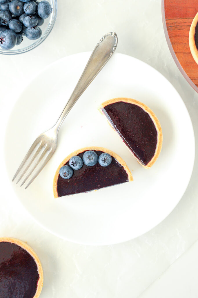 Blueberry Tart on a plate with a fork, sliced in half