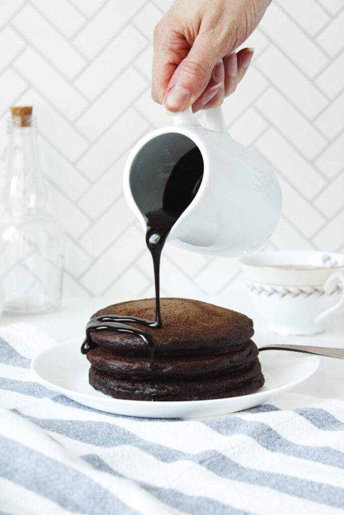 Drizzling chocolate sauce on a stack of three Chocolate Pancakes